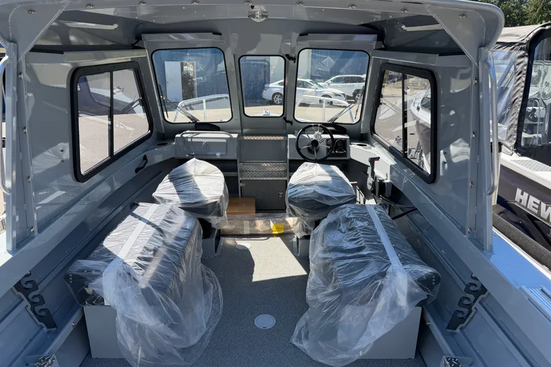 Slide: The Image of The image shows the interior of a Hewescraft 180 ProV Hard Top boat. It features an enclosed cabin with two seats wrapped in plastic and a steering wheel at the front. - 5