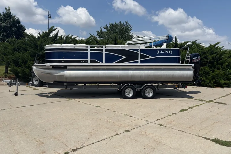 The Image of 2020 Lund LX220 Pontoon boat on trailer, parked outdoors under a cloudy sky. - 0