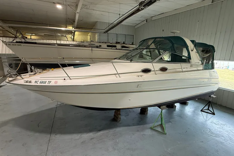 The Image of 1998 Sea Ray 290 Sundancer boat in indoor storage, featuring a sleek design and green canopy. - 0