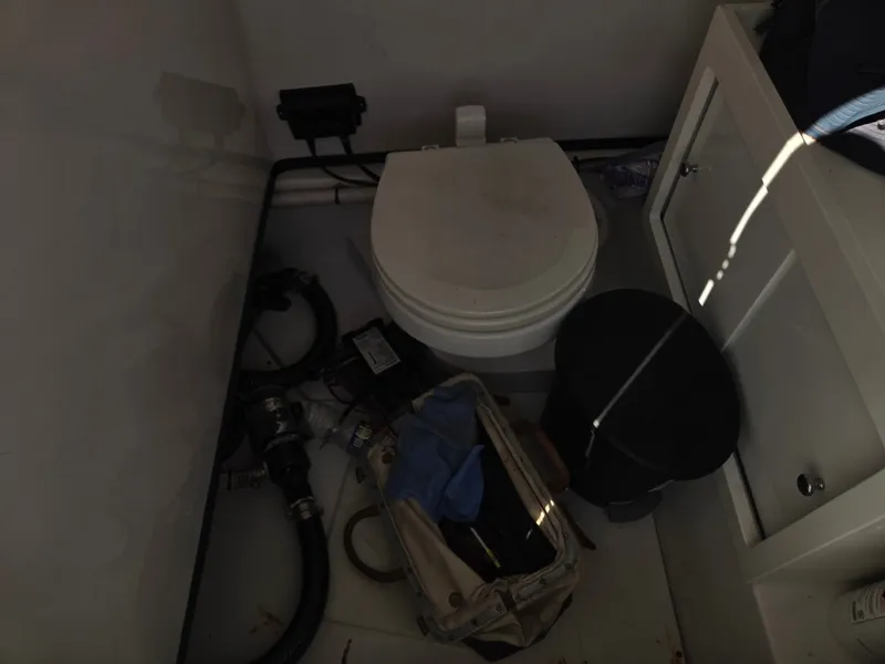 Slide: The Image of A small bathroom with a toilet, a black bucket, and some pipes on the floor. - 15