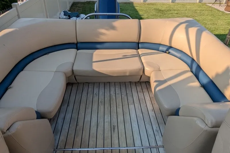 Slide: The Image of 2017 Manitou 23 Aurora VP boat interior with beige and blue seating on wooden deck. - 3