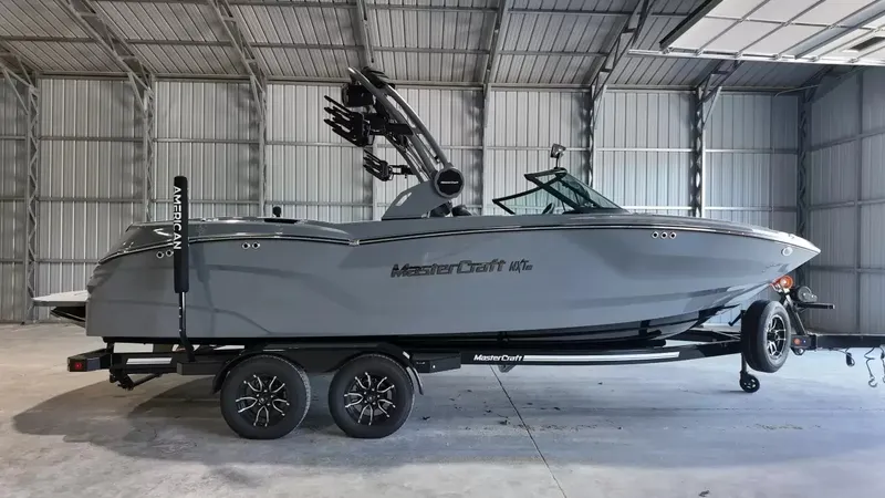The Image of A gray 2027 MasterCraft NXT23 boat on a trailer inside a warehouse. - 1
