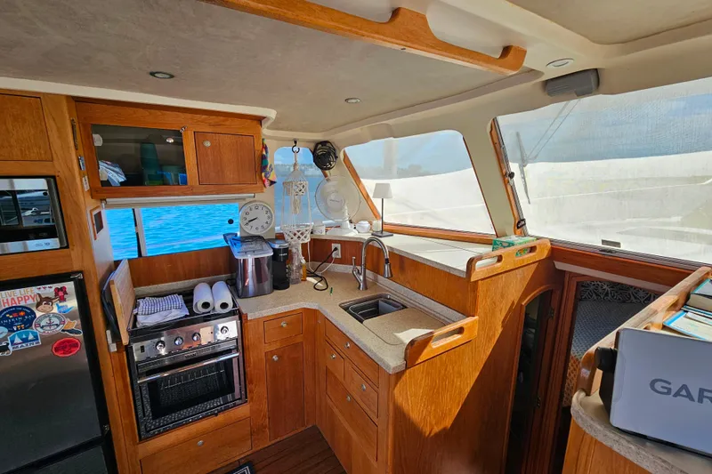 Slide: The Image of Interior of 2000 Mainship 39 Trawler, featuring a well-equipped kitchen with wooden cabinetry. - 49
