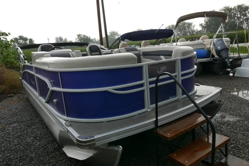 Slide: The Image of 2023 Barletta Cabrio 22UC pontoon boat with blue exterior, parked on gravel. - 1