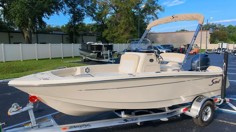 The Image of Scout 188 Sportfish 2027 on a trailer, cream-colored, with a bimini top and outboard motor. - 1