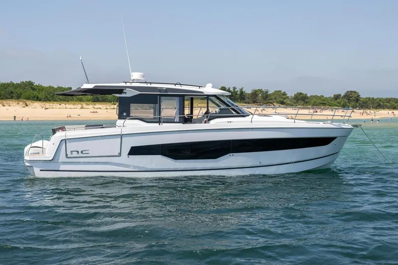 Slide: The Image of Manufacturer Provided Image: 2025 Jeanneau NC 1295 Coupe yacht on calm waters near a sandy beach. - 1