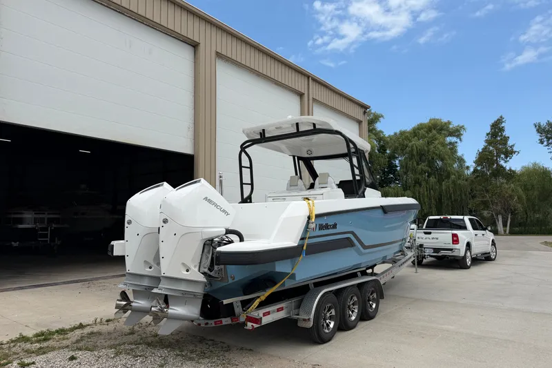 Slide: The Image of 2027 Wellcraft 28 T-Top boat on trailer, parked outside a large garage. - 3