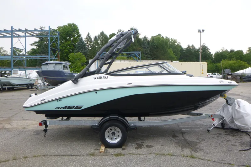 The Image of 2026 Yamaha Boats AR195 on trailer, parked outdoors with trees in background. - 1