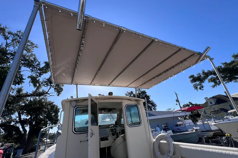 Slide: The Image of 2012 Parker 2320 SL Sport Cabin boat with canopy, docked under clear blue sky. - 17