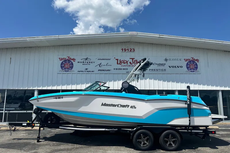 The Image of 2024 MasterCraft NXT22 boat on trailer outside dealership building. - 1
