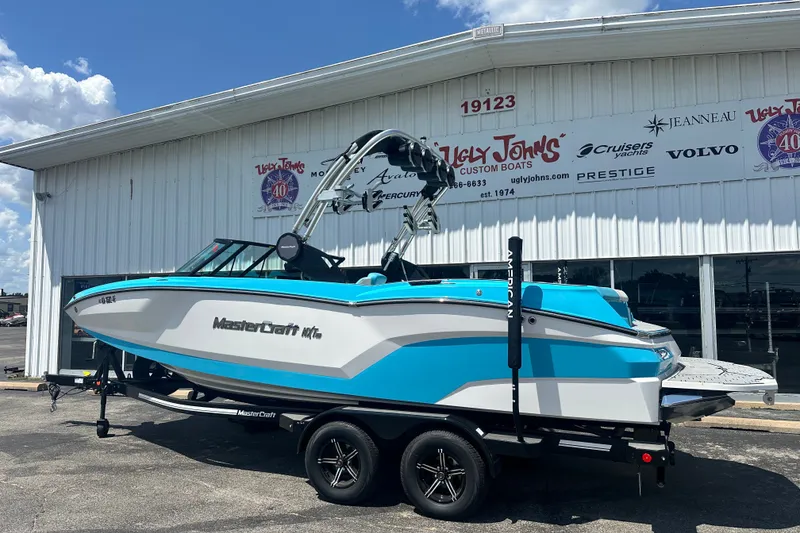 Slide: The Image of 2024 MasterCraft NXT22 boat in blue and white on a trailer outside a dealership. - 2