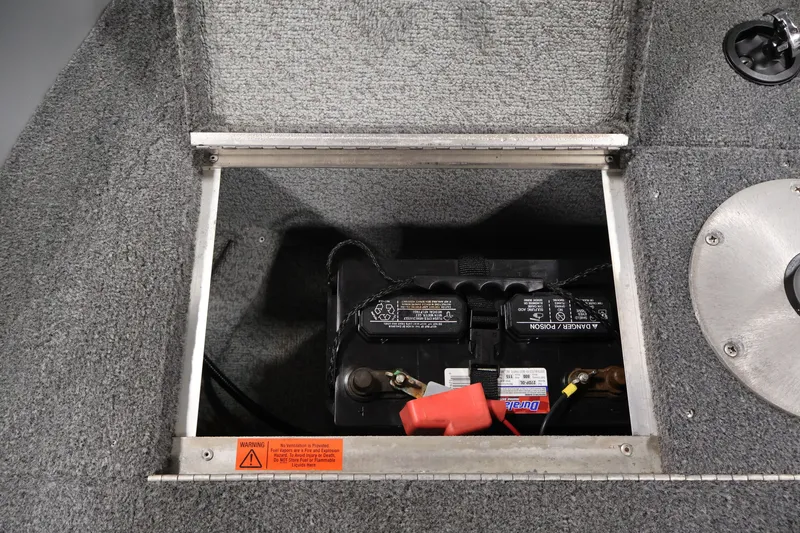 Slide: The Image of Battery compartment of 2004 Alumacraft Navigator 165 CS boat, showing secured battery and warning label. - 17