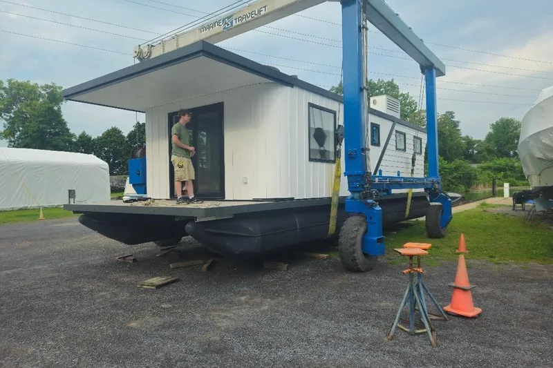 Slide: The Image of 2026 East Coast Houseboats Cayuga model on a trailer, with a person standing on deck. - 14