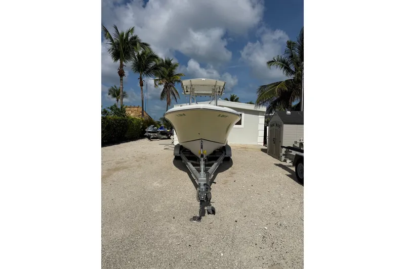 Slide: The Image of 2006 Sailfish 2360 CC boat on trailer, parked near palm trees and a white building. - 2
