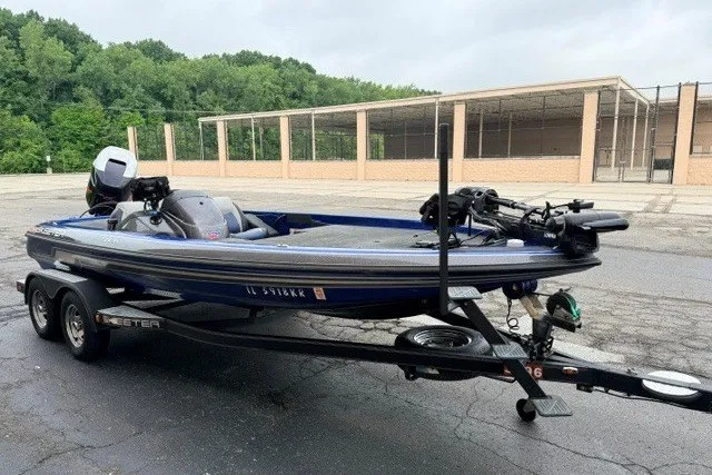 Slide: The Image of 2014 Skeeter TZX195 bass boat on trailer, parked outdoors near trees and a building. - 5