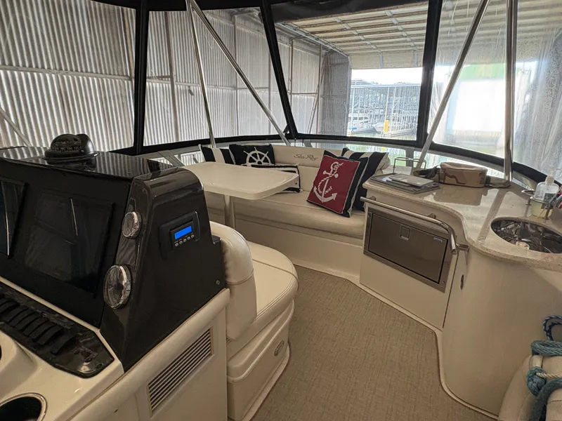 Slide: The Image of The image shows the cockpit of a 2008 Sea Ray 47 Sedan Bridge. There's a white bench with decorative pillows, a table, and a helm with instruments. - 16