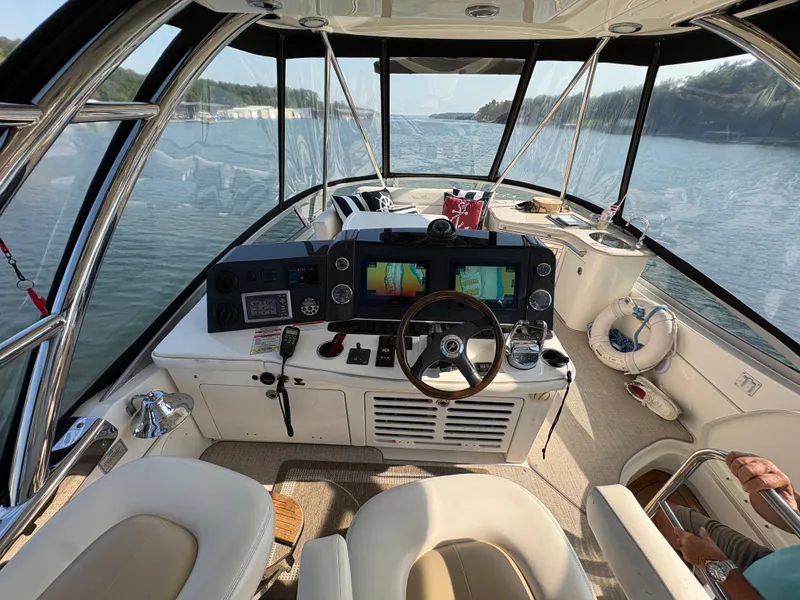 Slide: The Image of The image shows the cockpit of a 2008 Sea Ray 47 Sedan Bridge. It features a sleek design with a wooden steering wheel, modern instruments, and comfortable seating. The view of the water through large windows is impressive. - 25