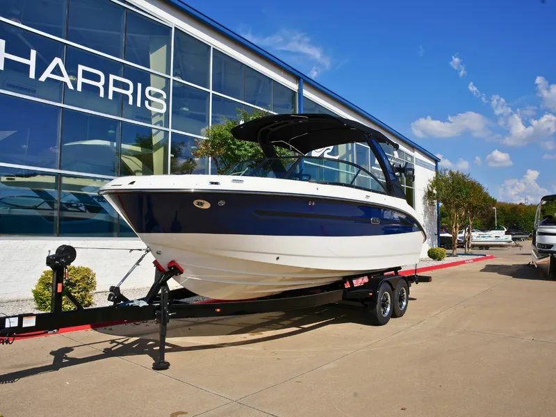 Slide: The Image of A 2027 Sea Ray SDX 250 Surf on a trailer in front of a modern building. - 1