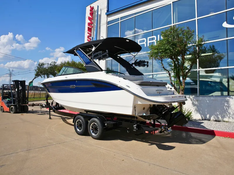 Slide: The Image of A 2027 Sea Ray SDX 250 Surf on a trailer in front of a modern building. - 2