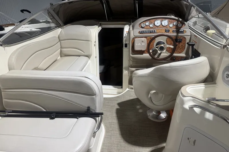 Slide: The Image of 2006 Larson Cabrio 260 boat interior with beige seating and wood-accented dashboard. - 18