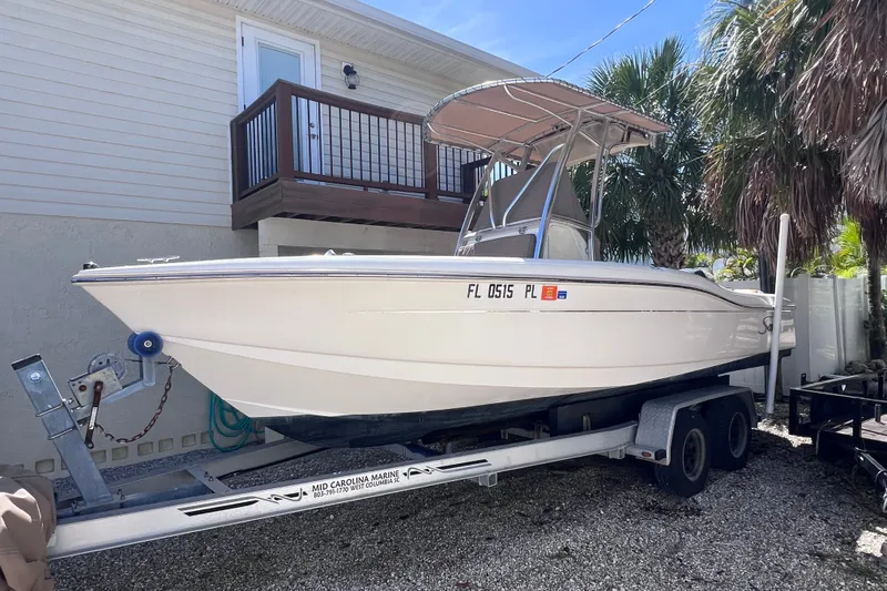The Image of 2012 Scout 210 XSF boat on trailer, parked beside a house with palm trees. - 0