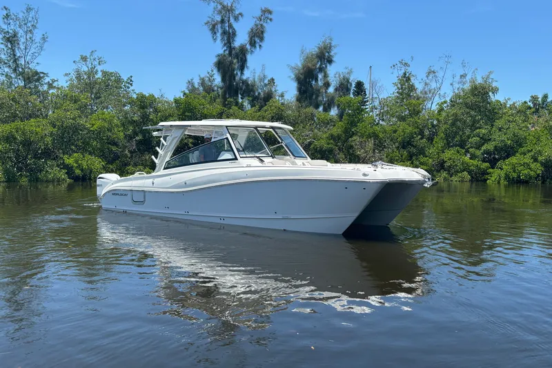 Slide: The Image of 2027 World Cat 325 DC boat on calm water, surrounded by lush greenery. - 1