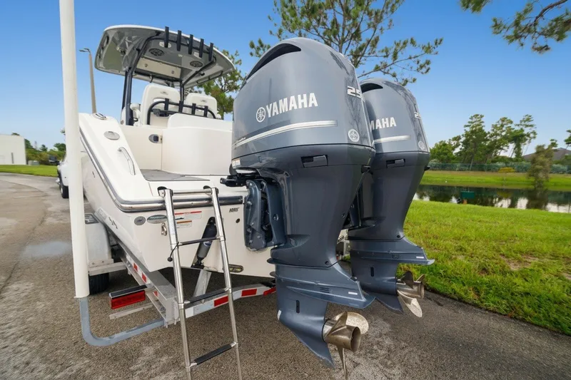 Slide: The Image of 2021 Cobia 280 Center Console with twin Yamaha outboard engines, parked near a pond. - 16