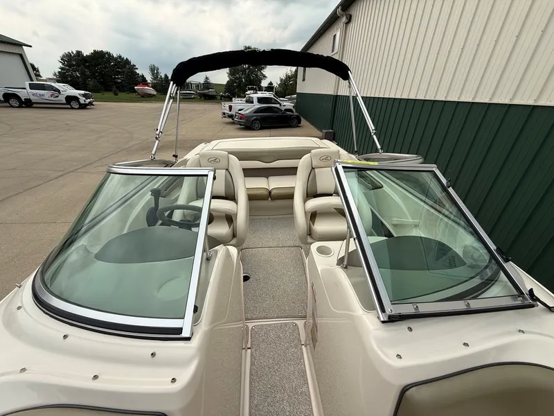 Slide: The Image of A 2005 Sea Ray 200 Sport with beige interior and black bimini top, parked beside a building. - 12