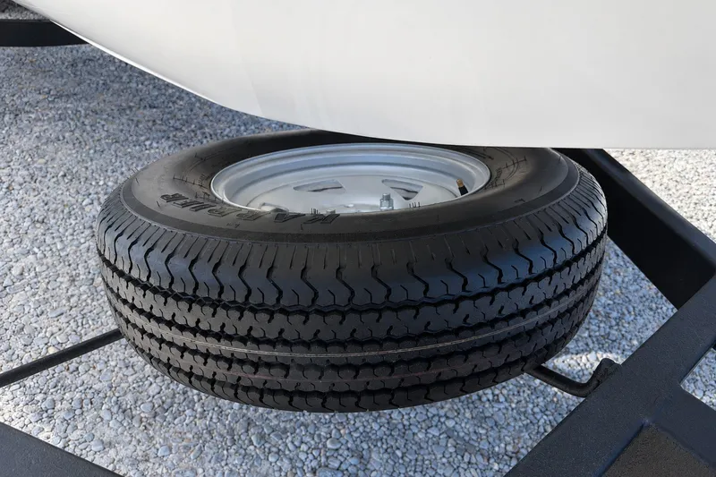 Slide: The Image of Spare tire mounted on a 2022 Tahoe 2150 trailer, resting on gravel. - 38