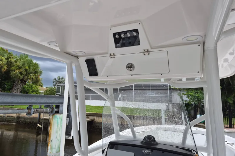 Slide: The Image of 2023 Sea Fox 268 Commander boat console with storage and controls, docked near lush greenery. - 13
