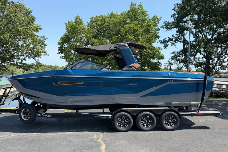 Slide: The Image of 2026 Nautique Super Air Nautique G25 boat on trailer, parked near trees. - 3