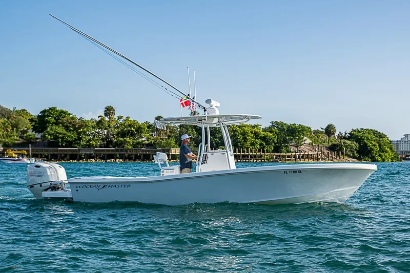 Slide: The Image of 2019 Ocean Master 296 boat cruising on blue water near lush shoreline. - 0