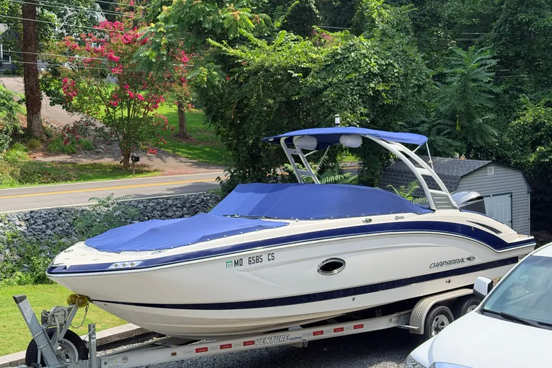 The Image of 2016 Chaparral 250 Suncoast boat on trailer, covered, surrounded by lush greenery. - 1