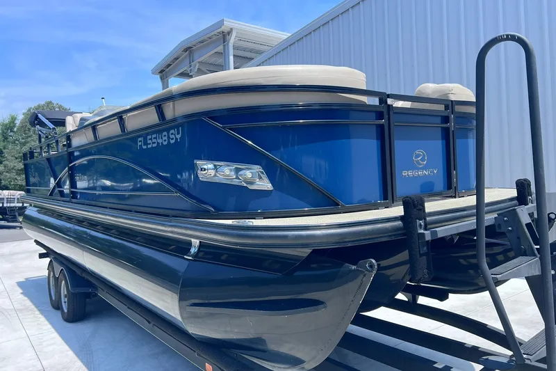 Slide: The Image of 2020 Regency 250 DL3 pontoon boat on trailer, blue exterior, parked outdoors. - 2