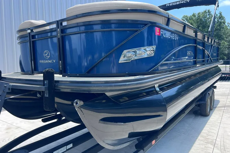 Slide: The Image of 2020 Regency 250 DL3 pontoon boat in blue, parked on a trailer. - 4