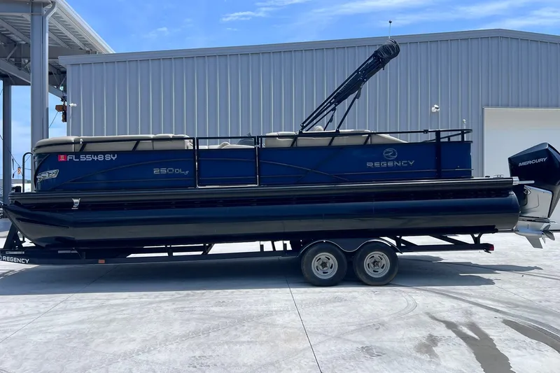 Slide: The Image of 2020 Regency 250 DL3 pontoon boat on trailer, parked outdoors near a building. - 5