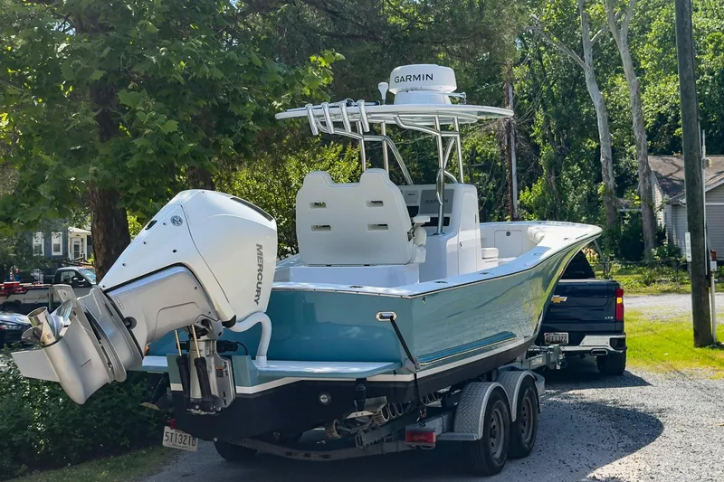 Slide: The Image of 2025 Weaver 25 boat on trailer, featuring Mercury outboard engine and Garmin radar, in a wooded area. - 2