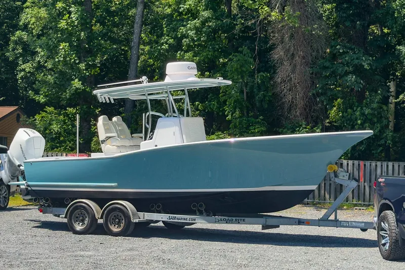 The Image of 2025 Weaver 25 boat on trailer, parked outdoors with lush green trees in background. - 0