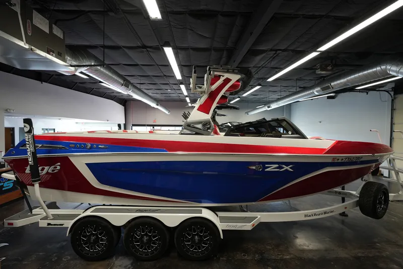 Slide: The Image of 2021 Tigé 25ZX boat in showroom, red and blue design on trailer. - 6