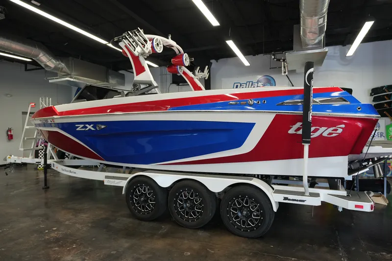 Slide: The Image of 2021 Tigé 25ZX boat in showroom, featuring red, blue, and white design on trailer. - 10