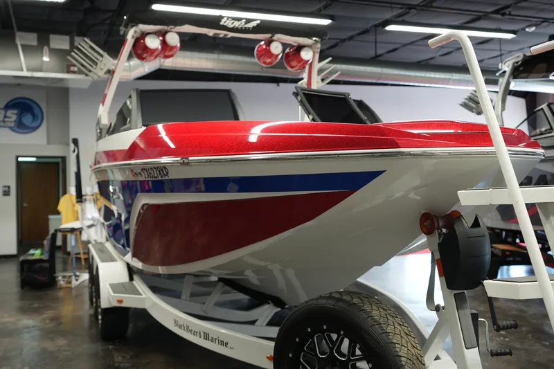 Slide: The Image of 2021 Tigé 25ZX boat in showroom, featuring red, white, and blue design on trailer. - 7