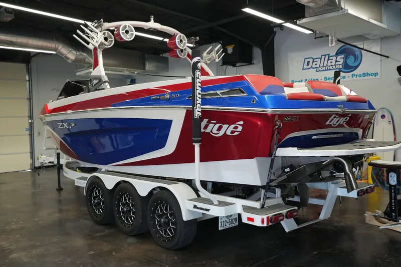 Slide: The Image of 2021 Tigé 25ZX boat in showroom, red and blue design, on trailer. - 2