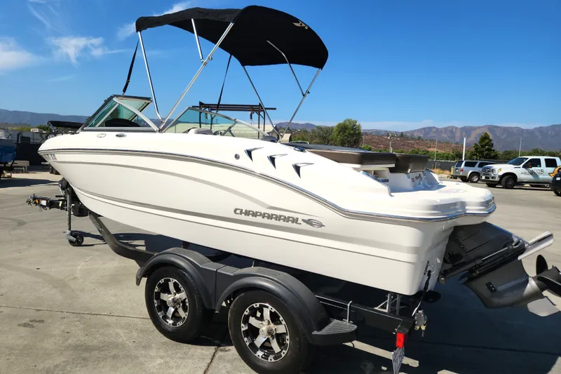 Slide: The Image of 2020 Chaparral 19 SSi boat on trailer, parked outdoors under clear blue sky. - 12