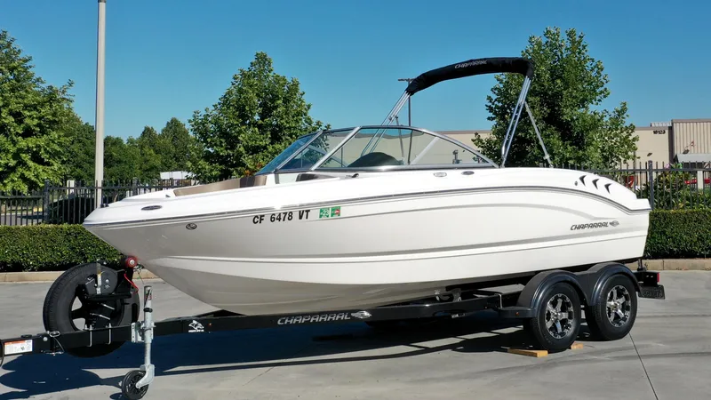 The Image of A white 2020 Chaparral 19 SSi boat on a trailer, surrounded by trees and buildings. - 1