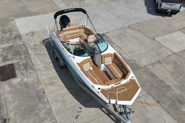 Slide: The Image of 2025 NauticStar 243 DC Deck boat on trailer, featuring spacious seating and sleek design. - 2
