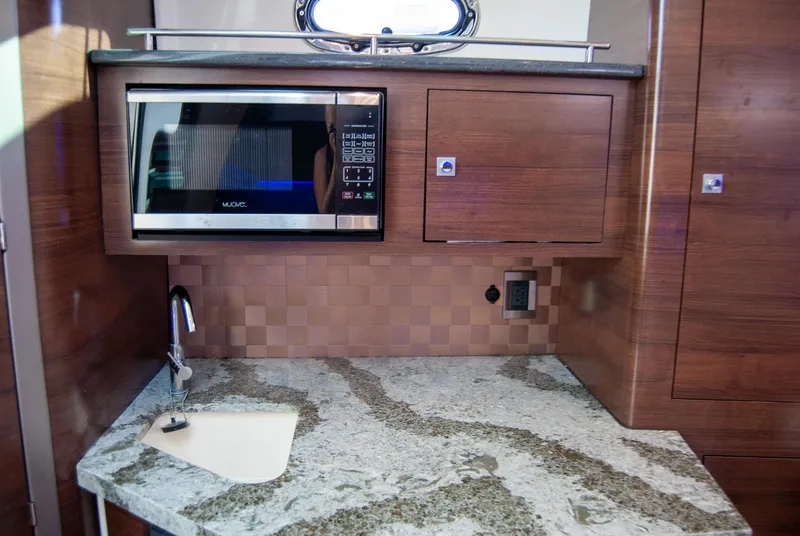 Slide: The Image of 2021 Boston Whaler 345 Conquest galley with microwave, sink, and wood cabinetry. - 28
