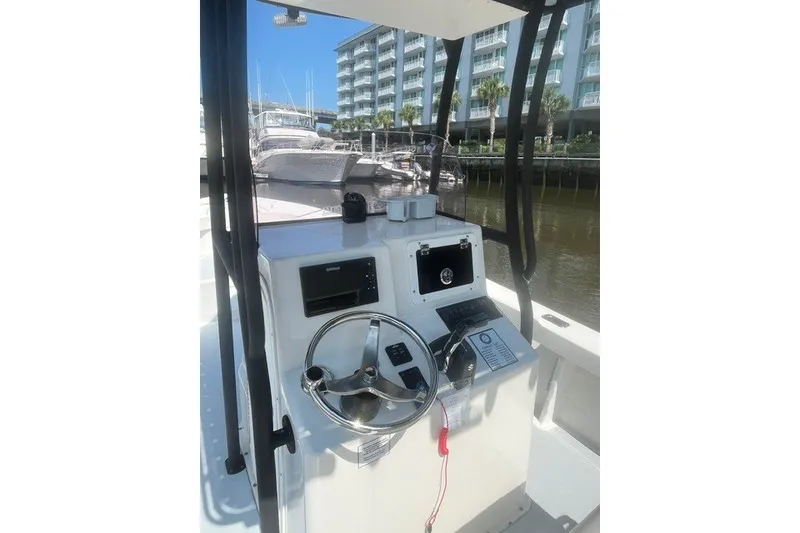 Slide: The Image of 2022 May-Craft 2300CC boat console with steering wheel and controls, docked near waterfront buildings. - 4