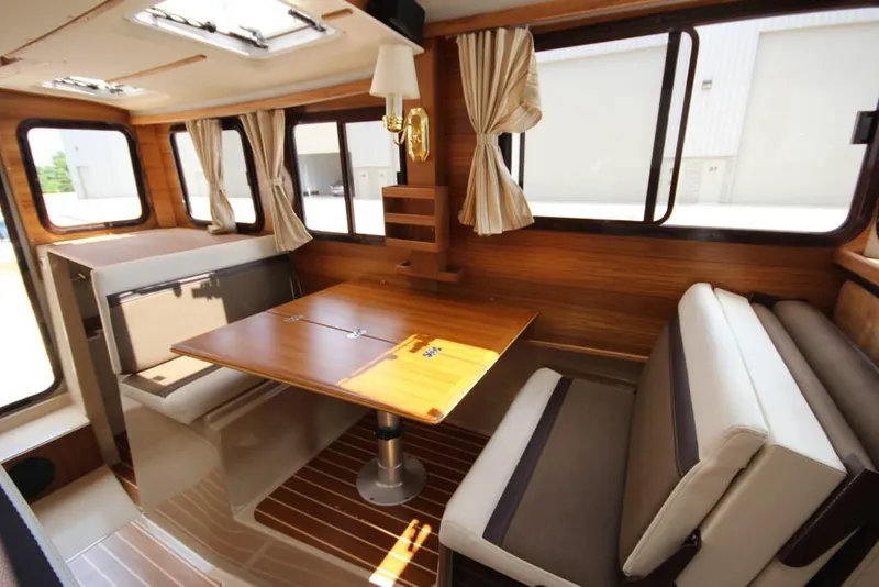 Slide: The Image of Interior of the 2015 Ranger Tugs R-27 with a wooden table, cushioned seating, and curtained windows. - 23