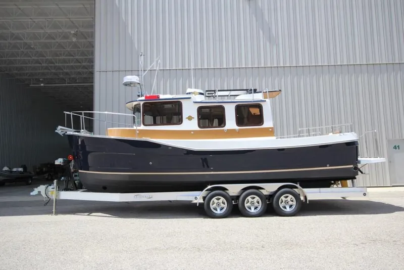 The Image of A 2015 Ranger Tugs R-27 on a trailer in front of a large building. - 0