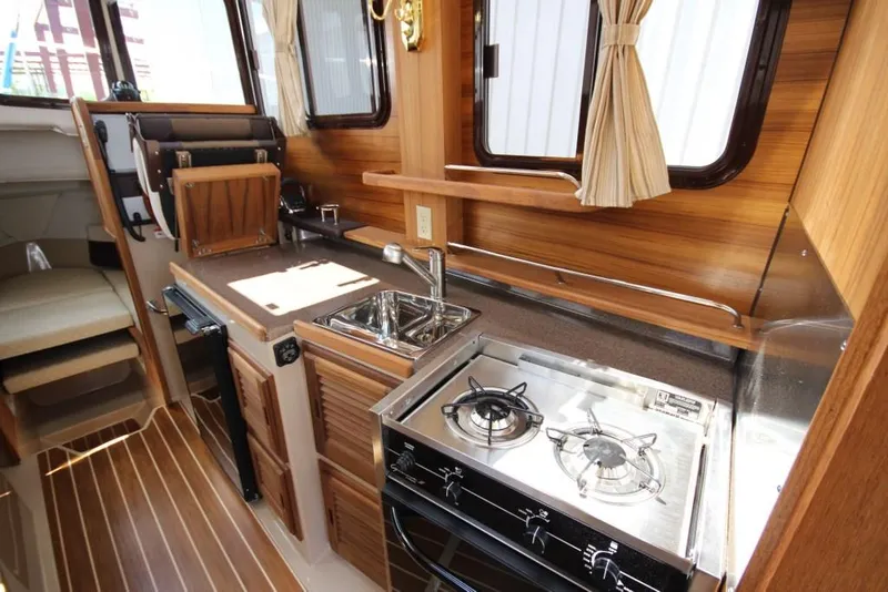 Slide: The Image of The galley of a 2015 Ranger Tugs R-27 with a stove, sink, and wood paneling. - 24